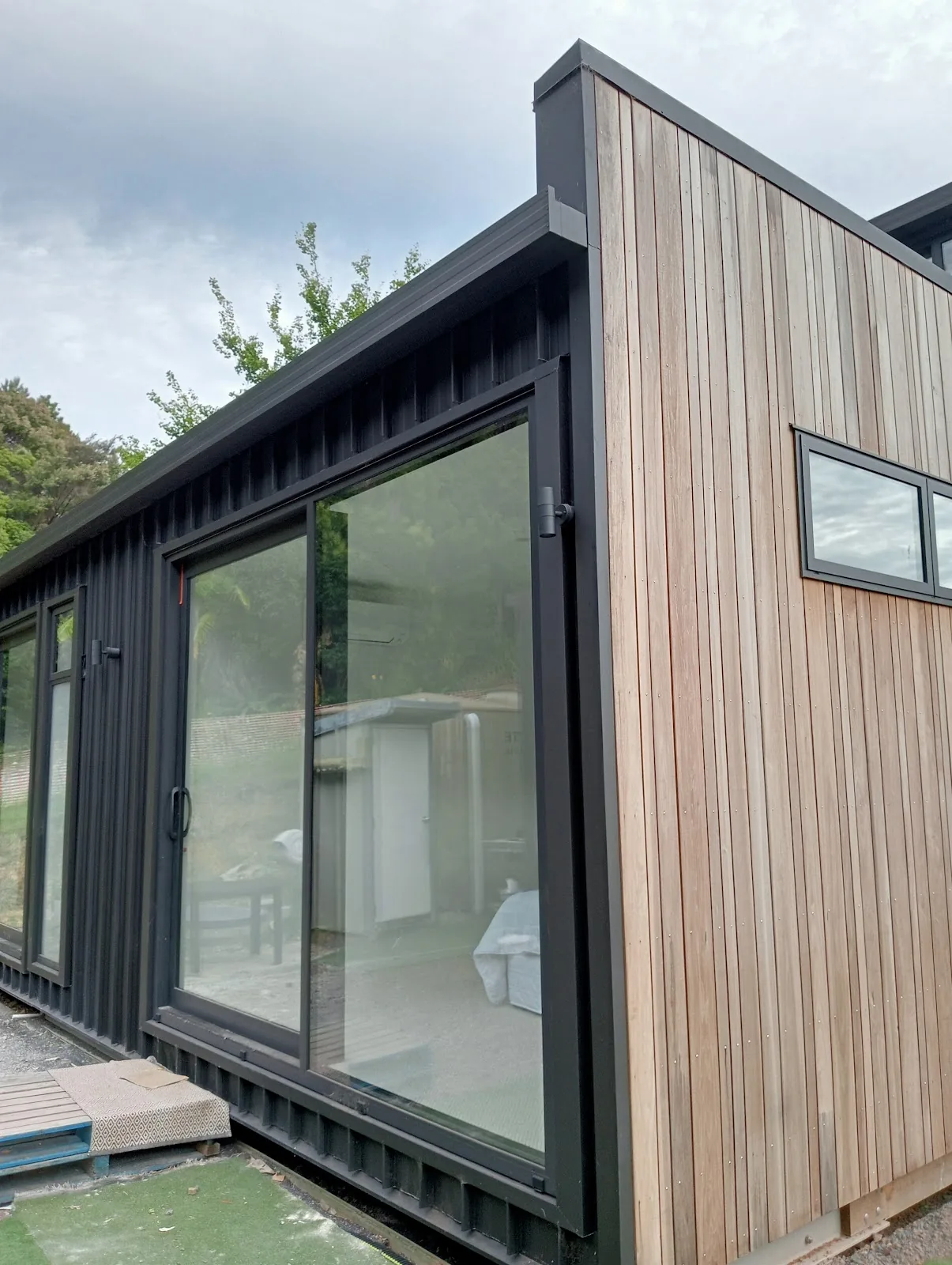 A timber clad cabin with tall black framed sliding doors and a high window